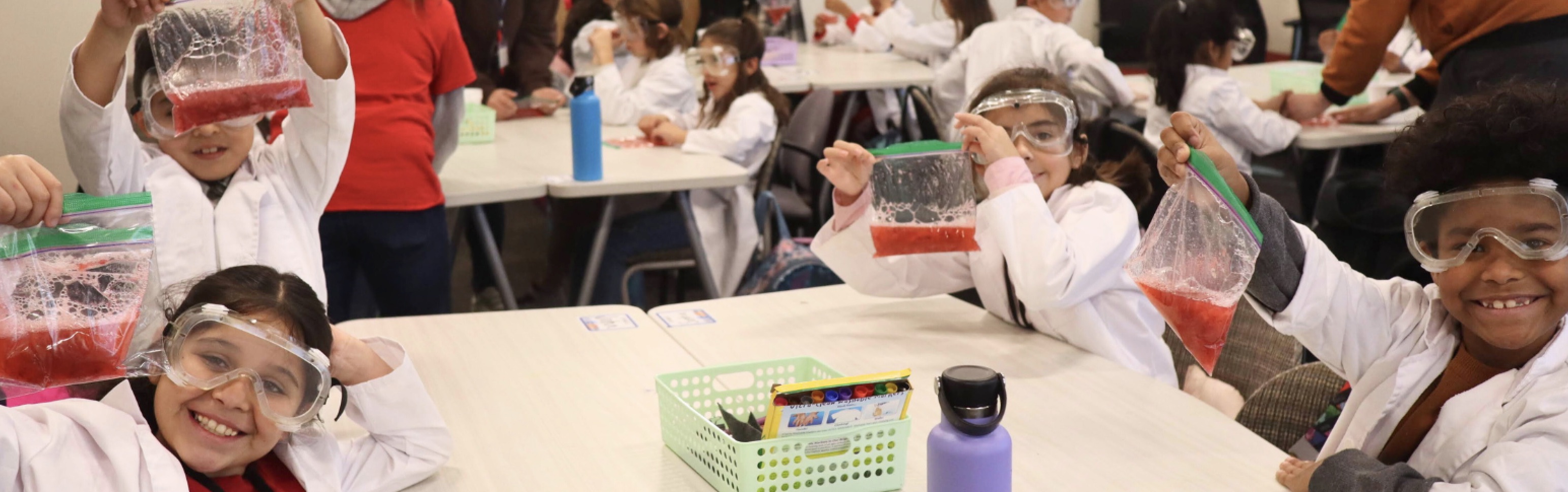 Science students in lab coats and goggles showing their ziploc bag experiments to the camera