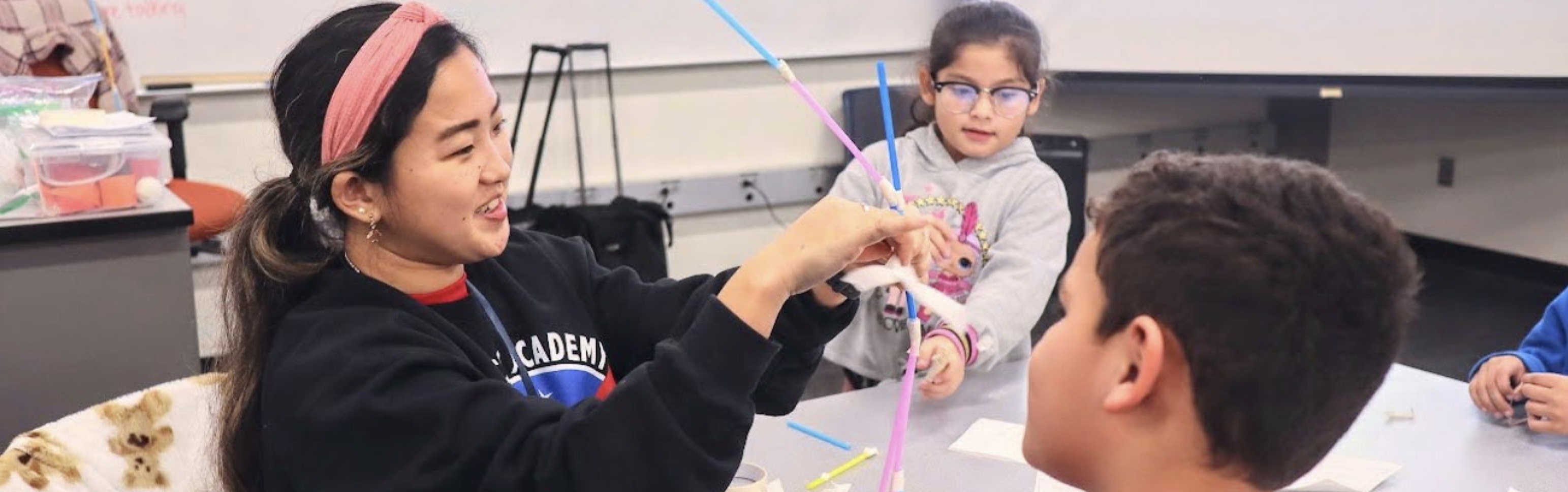 STEAM tutor helping students build a straw figurine