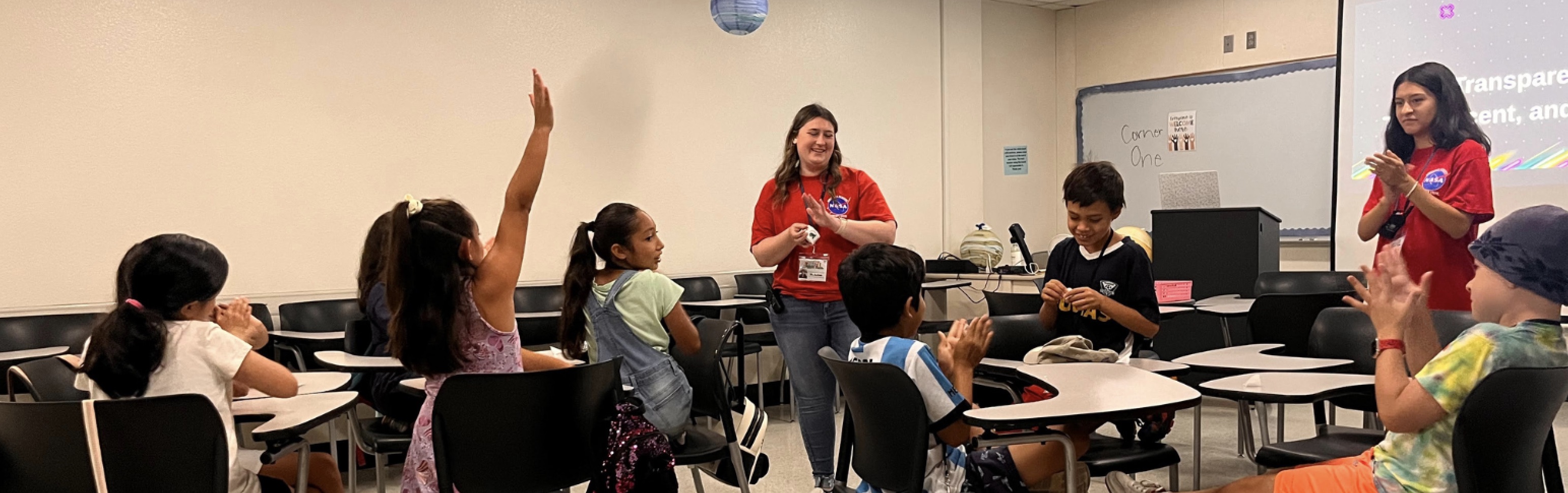 Students and tutors in class with students raising hands to answer questions