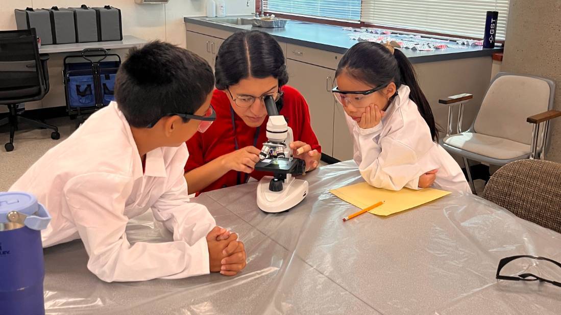 tutor with science students helping them examine a microscope