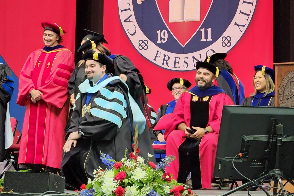 Zachary Rocca getting hooded at 2022 Commencement by his dissertation chair, Dr. Trang Phan