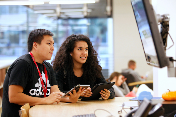 students hold tablets whiile looking at a screen