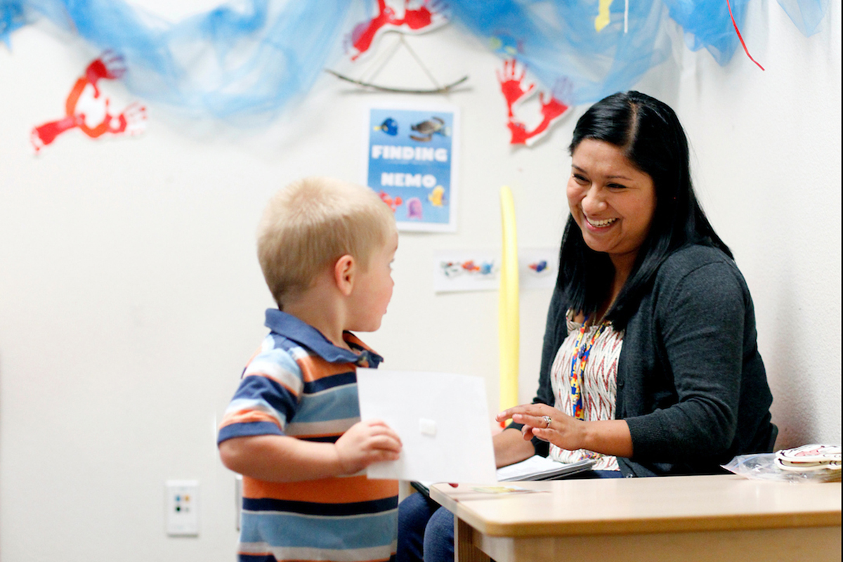 A young student shows a his work to a smiling teacher.