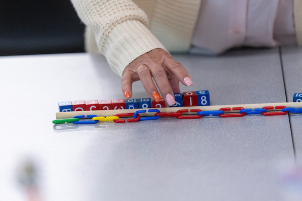 A teacher's hand lines up number blocks and a multi-colored plastic chain.